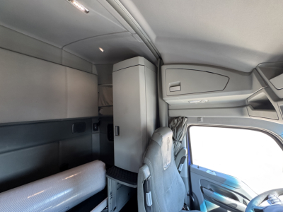 Kenworth T680 cabin interior showing sleeper area and overhead storage with cabinet; driver seat in view and window to the right.