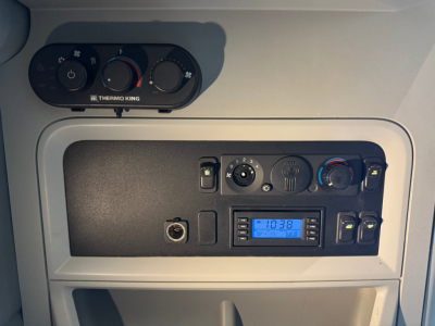 Dashboard panel in a Kenworth truck cab showing climate controls, power outlets, and an aftermarket stereo display. Visible text includes THERM KING logo and control labels.