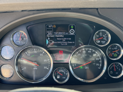 Dashboard of a Kenworth truck showing multiple gauges including rpm, speedometer, fuel gauge, and a central digital display with vehicle status icons.