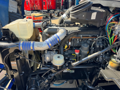 Kenworth T680 engine bay showing coolant reservoir, turbo hoses, and various fluid reservoirs.