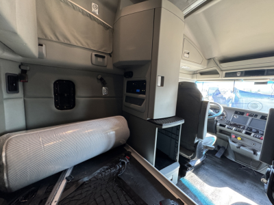 Cab interior of a 2019 Kenworth T680 in-view showing sleeper area with folded mattress, storage cabinet, and driver seat area; dashboard visible in right.