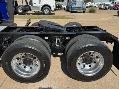 Dual rear axles and frame of a Kenworth truck chassis with chrome wheels and tires visible, no cab attached in this image.