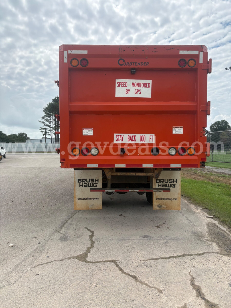 Rear view of a red Freightliner M2 106 dump truck showing 'Brush Hauq' mud flaps and warning labels.