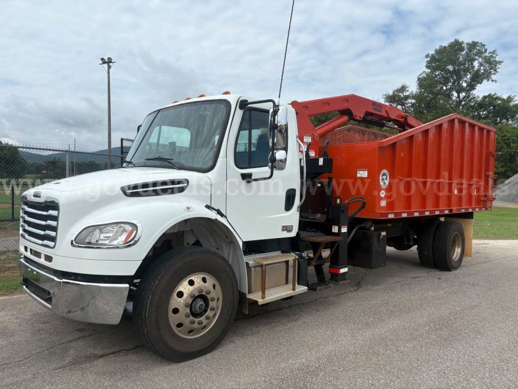 Freightliner M2 106 service truck with red dump body and boom crane, white cab, parked lot.