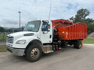 Freightliner M2 106 truck with white cab and red boom/dump body showing hydraulic arm and dump bed.