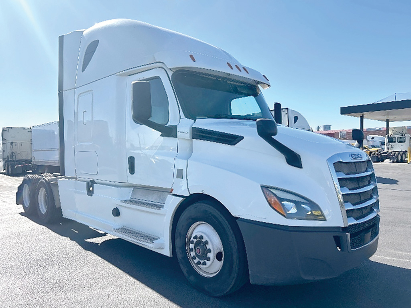 Freightliner Cascadia126: front left view showing long sleeper cab, white exterior, prominent grille, side mirrors, and dual rear axles.