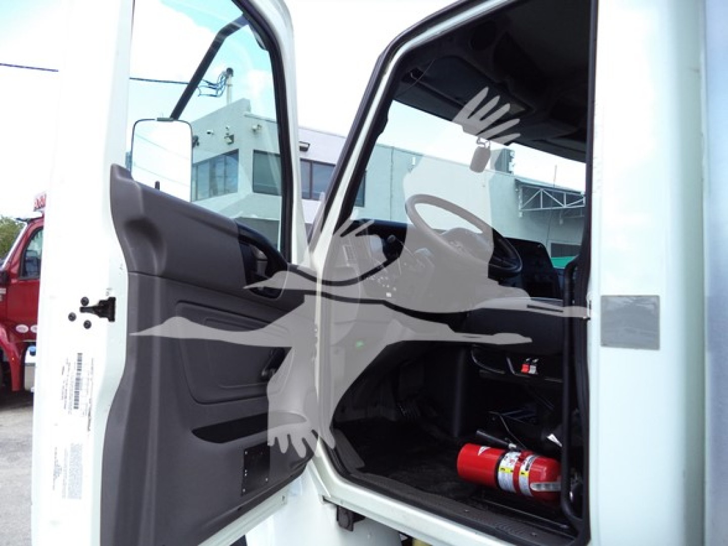Truck cab interior view with open door showing steering wheel and dashboard, fire extinguisher visible under dash area.