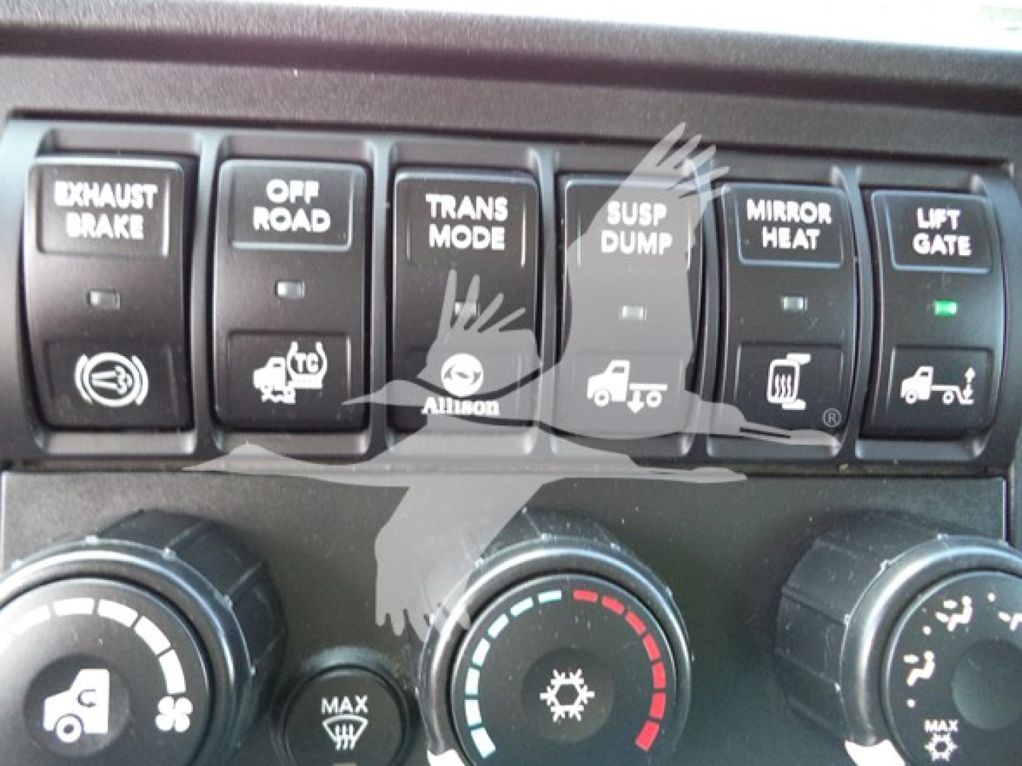 Dashboard controls showing exhaust brake, off-road, Trans mode, susp dump, mirror heat, lift gate switches and circular climate controls.