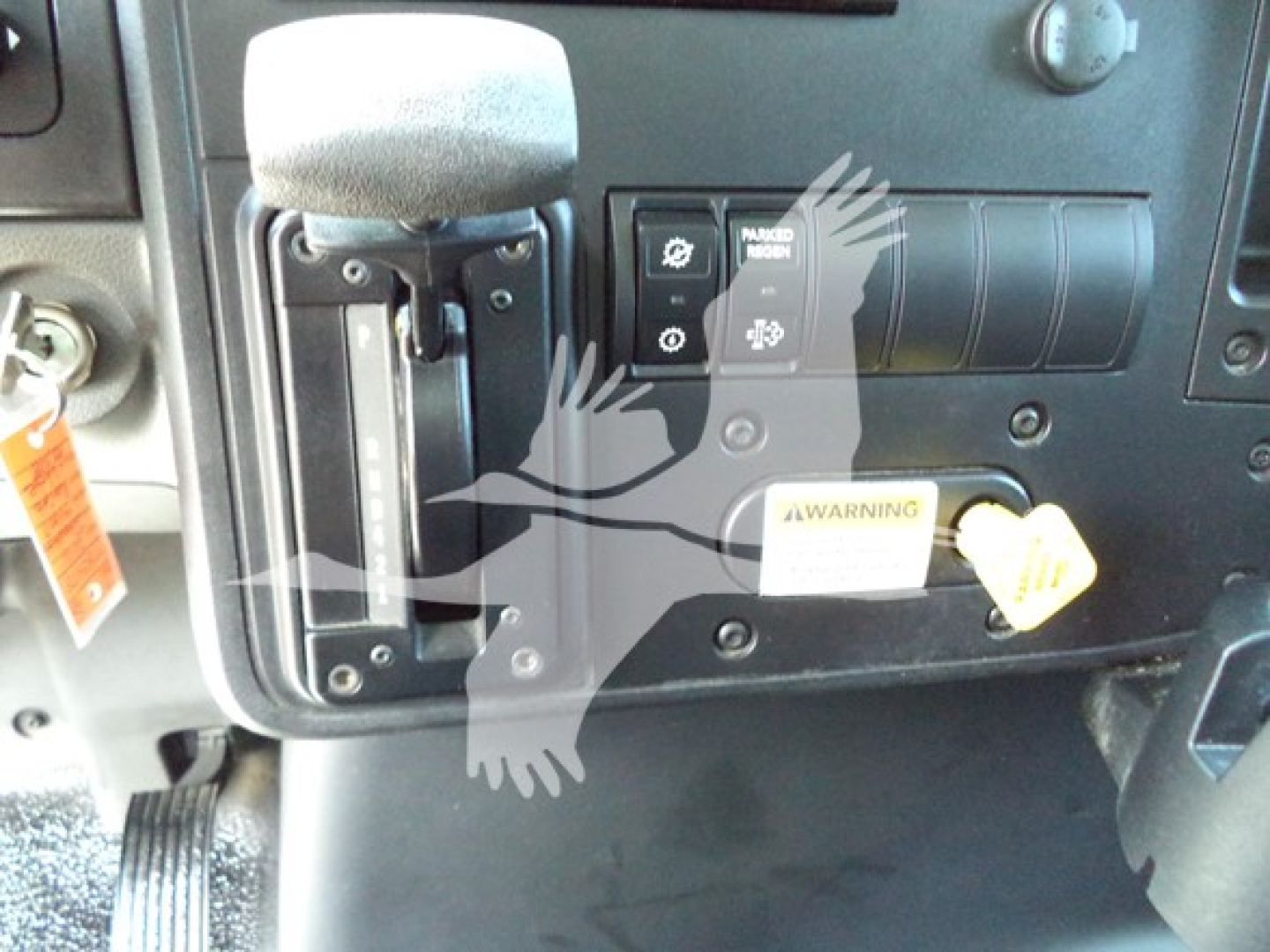 Dashboard area of 2021 International MV showing ignition switch, control switches, and gear selector with labels. Visible text includes warning label and small panels.