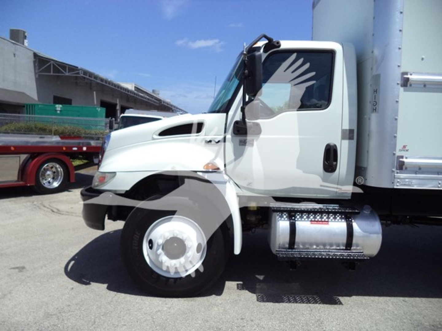 International MV truck cab and front wheel visible with box trailer, side view, white cab and silver fuel tank.