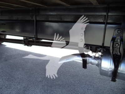 Trucks undercarriage showing drivetrain components and a mechanical shaft in the foreground with a stylized white bird watermark overlay.