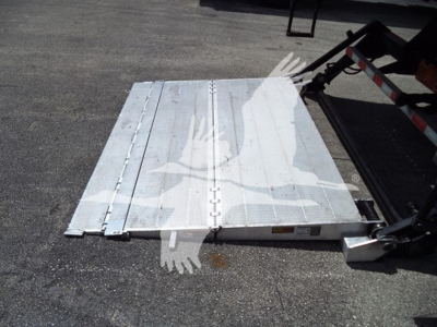 Platform with metal truck bed ramp or deck showing a light-gray aluminum surface, side hinges, and a hydraulic lift mechanism near the rear edge.