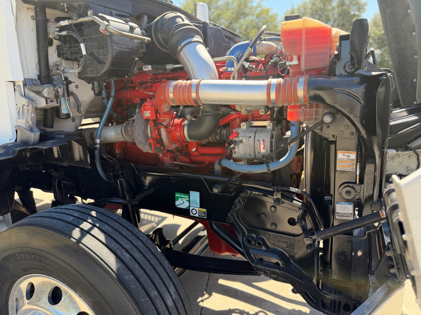 Kenworth T880 engine bay showing red engine block, intake piping, coolant reservoir, radiator at front, and chassis components.