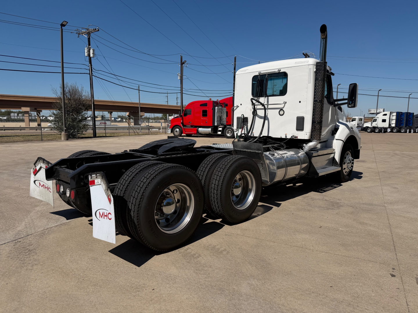 Kenworth T880 tractor rear and side view showing six-wheel configuration with white cab and chrome fuel tanks. Visible text includes MHC on rear mudflaps and multiple tires.