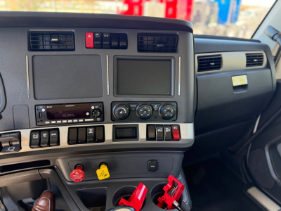 Kenworth T880 dashboard view showing center console, two screen panels, climate controls, hazard switch, and various switches with red and yellow labels.