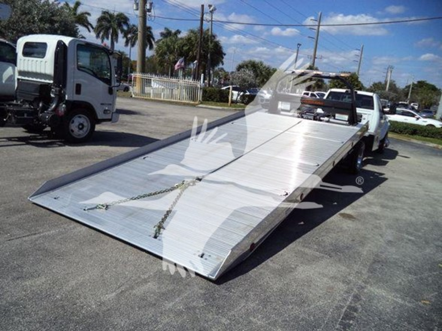 Ram 2026 Big Horn flatbed tow truck with a long aluminum ramp on a rollback bed, front cab visible in background.