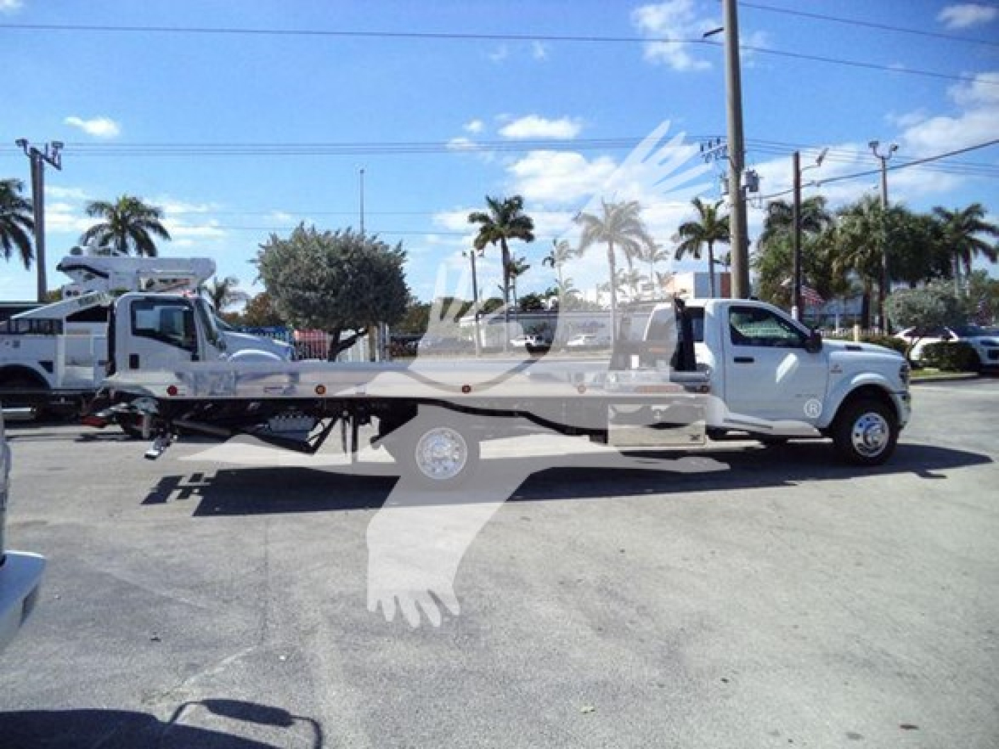 White Ram 5500 rollback tow truck with flatbed, side profile, dealership lot background and palm trees.