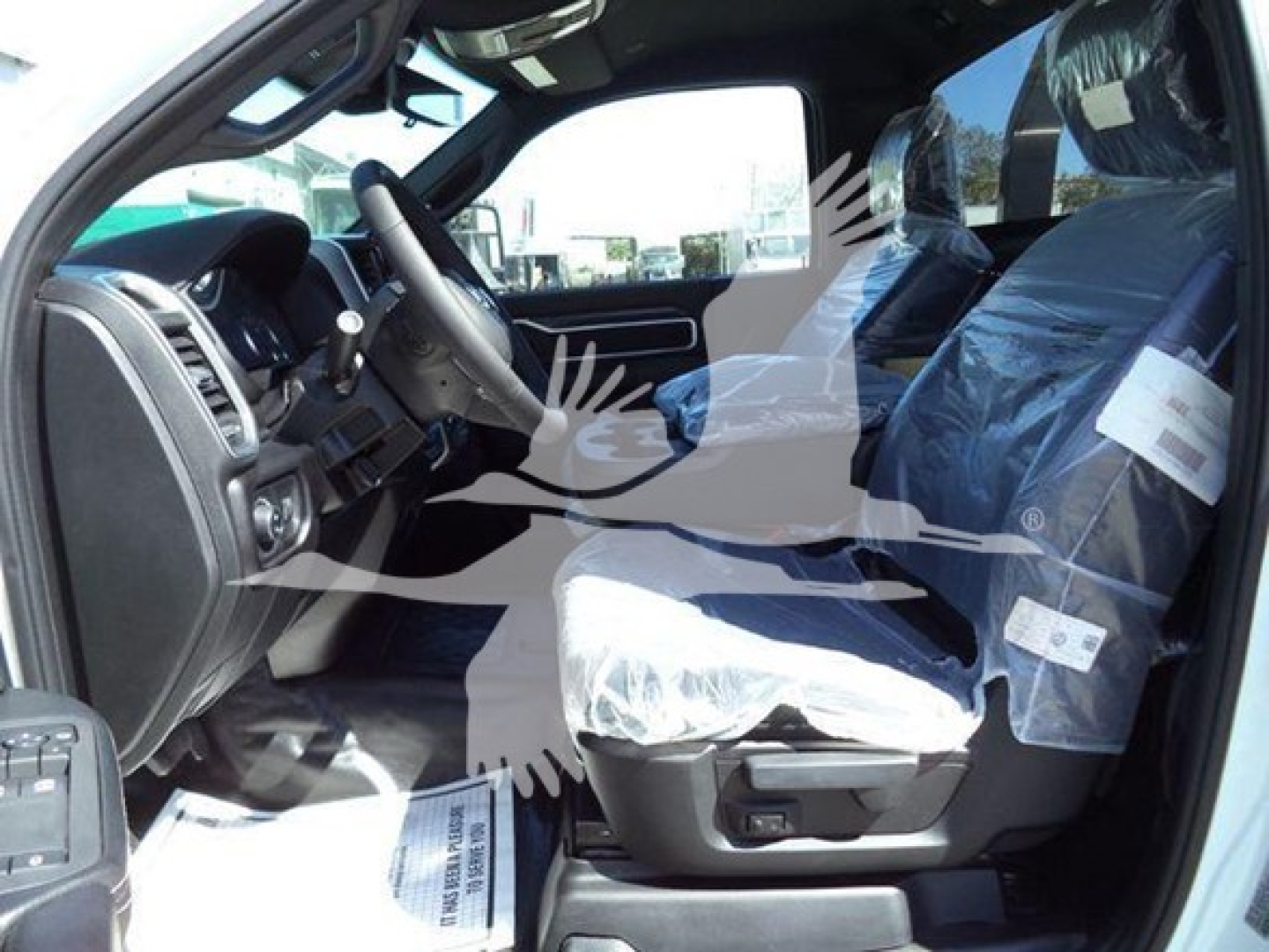 Truck interior of a new 2026 Ram Big Horn showing front seats wrapped in plastic, steering wheel, and dashboard from the driver’s side.
