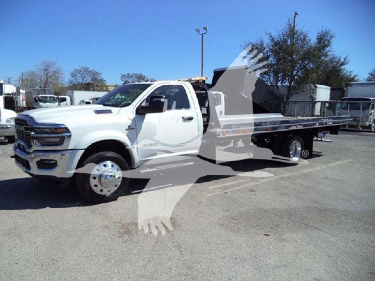 Truck in a showroom yard showing a white 2026 Ram Big Horn rollback w/ flatbed and tow setup, side view, dealership lot in background.