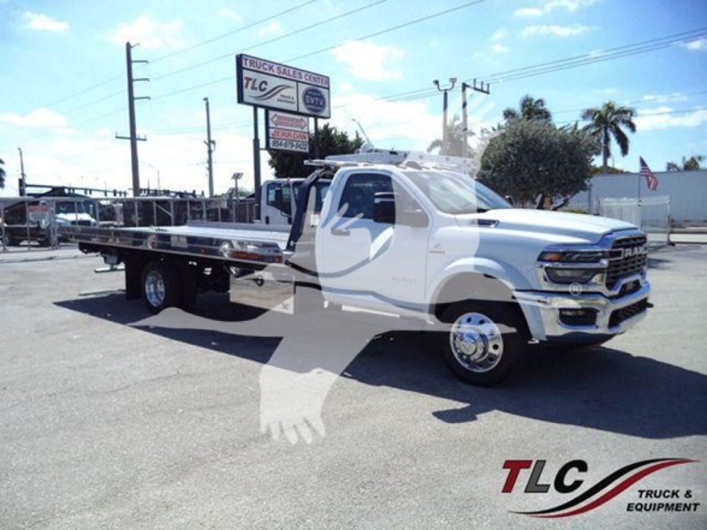 RAM truck with a rollback flatbed showing front grille and wheels, white cab, dealership signage in background.