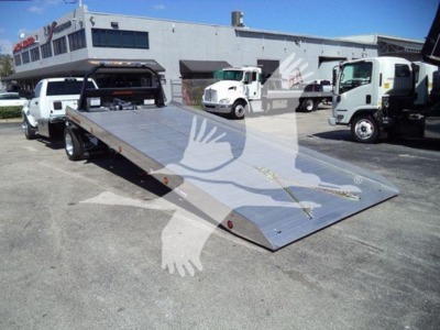 Ram 2026 Big Horn flatbed rollback truck in dealership lot showing aluminum tilt bed and Ram logo watermark