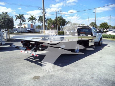 Flatbed tow truck from rear-left angle showing back of Ram pickup bed with hitch, in-service vehicle, clear sky, palm trees