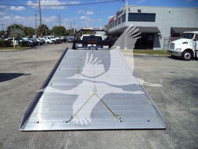 Truck rollback bed tilted ramp showing aluminum surface with hinge and chain, in dealership lot