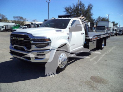 Ram tow truck flatbed showing 2026 Ram 5500/6500 style grille and wheels with rollback bed and winch in dealership lot, windows reflecting sun.