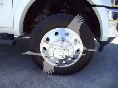 Truck front wheel well with chrome hub, Ram logo on center cap and wheel; partial side of white pickup with black step bar visible.