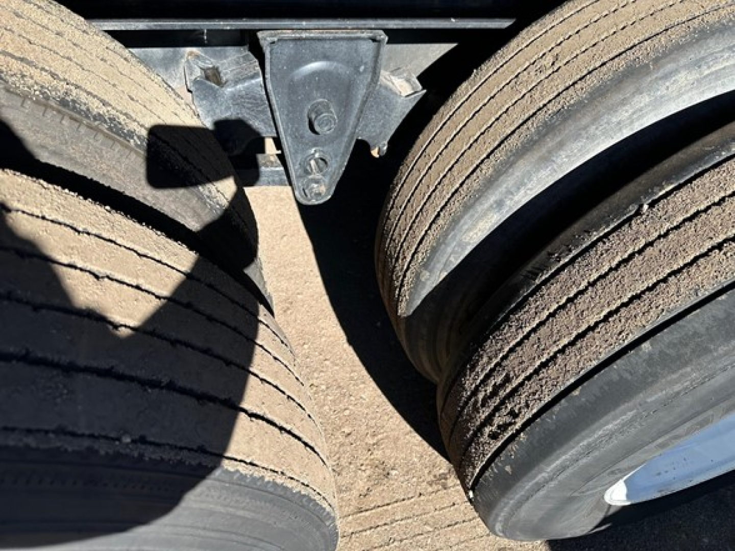 Flatbed trailer wheels and hub area showing dual tires and mud on tread, undercarriage components visible between wheels.