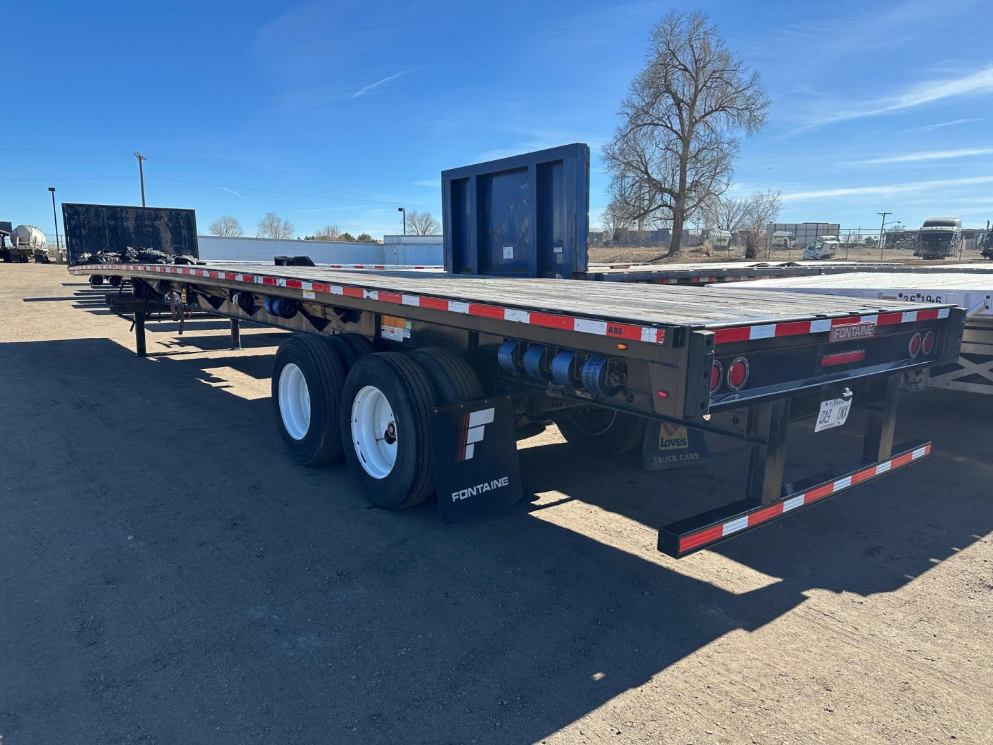 Fontaine Velocity flatbed trailer showing dual rear axles and black bed with white wheels and rear loading ramps visible.