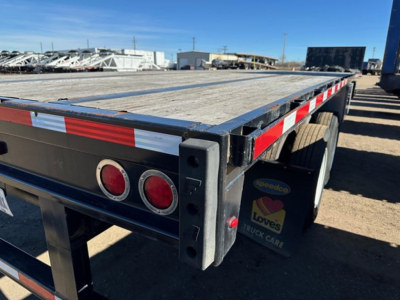 Flatbed trailer rear corner showing black frame with red marker lights and reflective tape; wooden deck; Speedco Loves support sticker visible.
