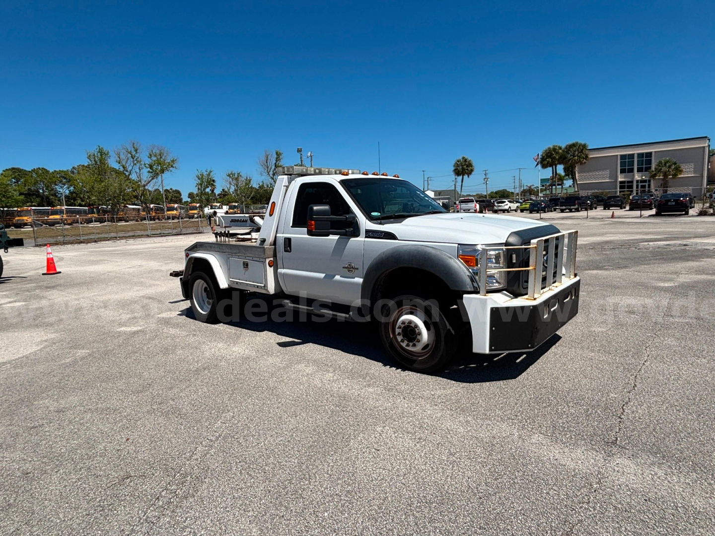 Ford F-550 tow truck in a parking lot, front-left view, silver with utility bed and amber clearance lights on roof.