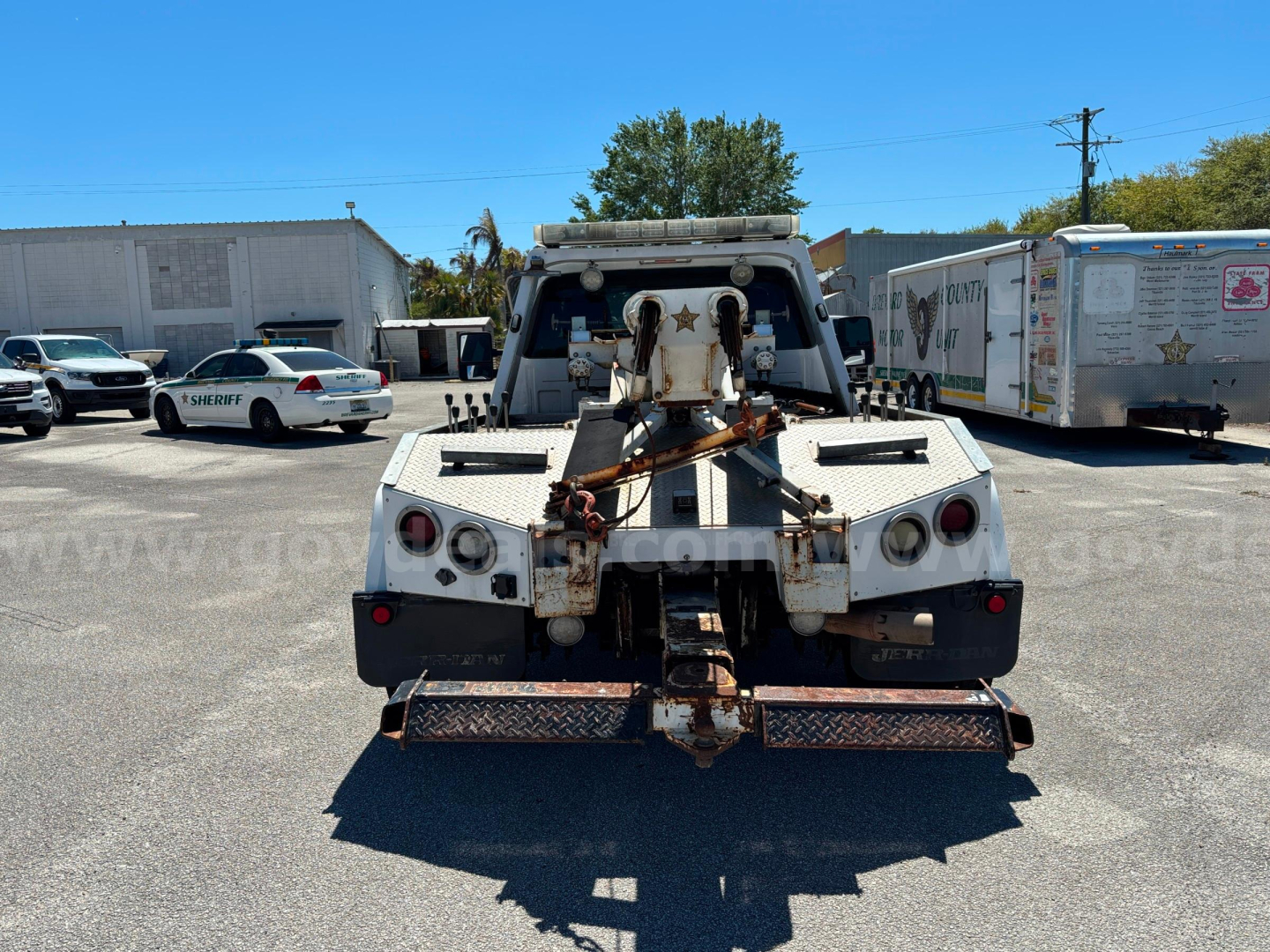 Tow truck rear with hitch and winch assembly, metal steps, and tail lights visible.