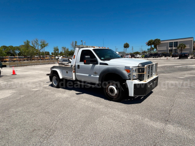 Ford F-550 tow truck in a parking lot, front-left view, silver with utility bed and amber clearance lights on roof.