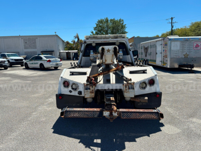 Tow truck rear with hitch and winch assembly, metal steps, and tail lights visible.