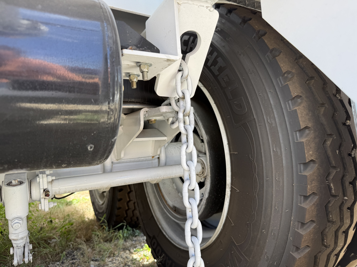 Trailer axle and tire with chain and hydraulic components visible in a tank trailer undercarriage.