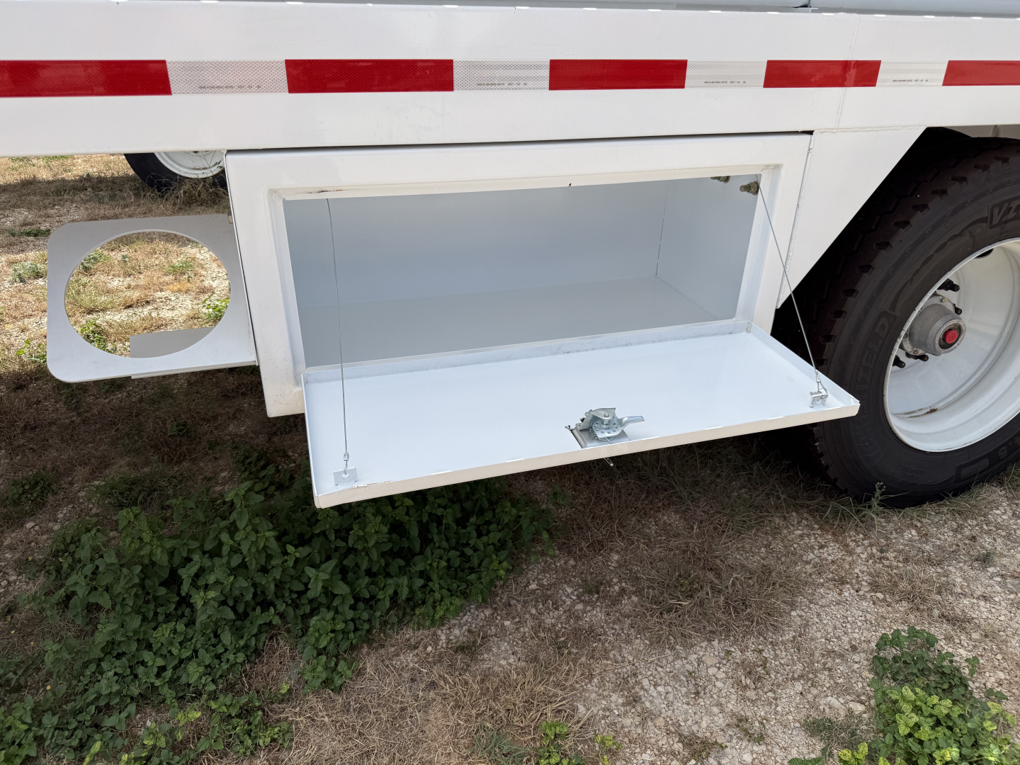 Trailer storage compartment open drawer under trailer showing white interior and latch, Iron Lite VAC130 trailer in background