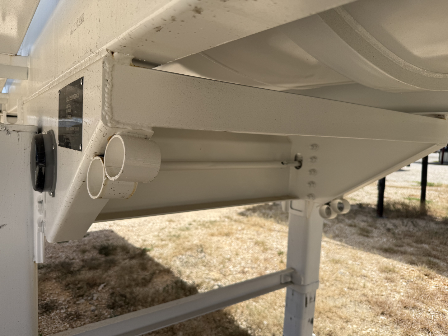 Trailer underside showing support beam, circular exhaust/indicator pipes, and frame joints on a white Iron Lite VAC130 trailer.
