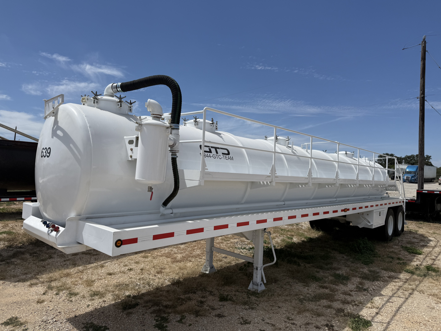 Trailer-mounted vacuum tanker tank showing white cylindrical vessel with raised hatch and black hose, side rails, support legs, and dual-axle undercarriage.