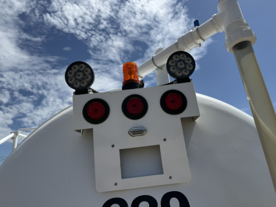 Tank trailer rear showing lights, reflectors, and small orange beacon on white panel; circular LED assemblies on top of the tank rear.