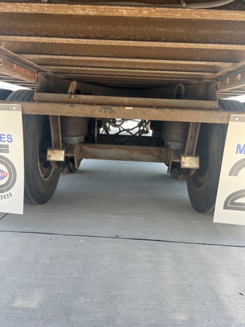 Trailer undercarriage showing axles, leaf springs, and frame of a 2013 utility van trailer with rust-tone metal and tires visible.