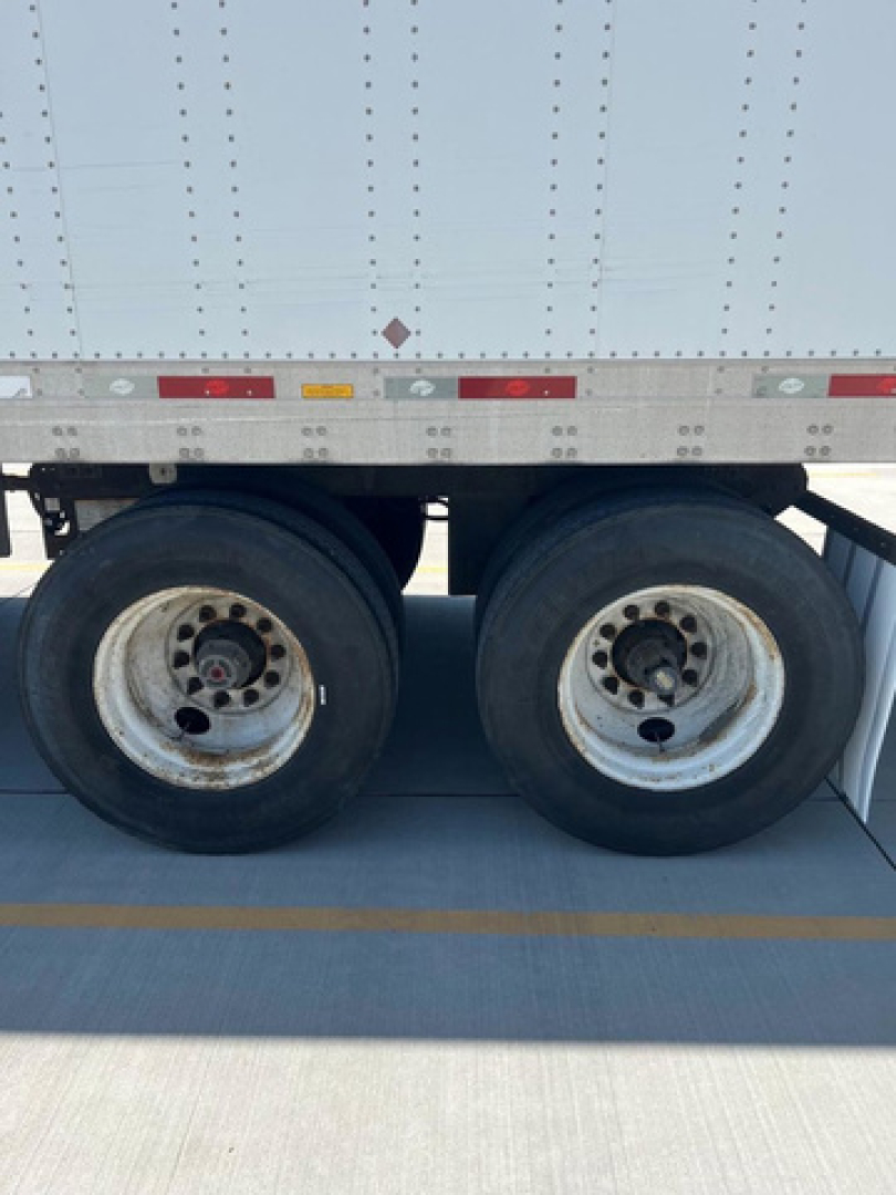 Dual rear wheels of a utility trailer with a white corrugated side, showing riveted panels and wheel rims.