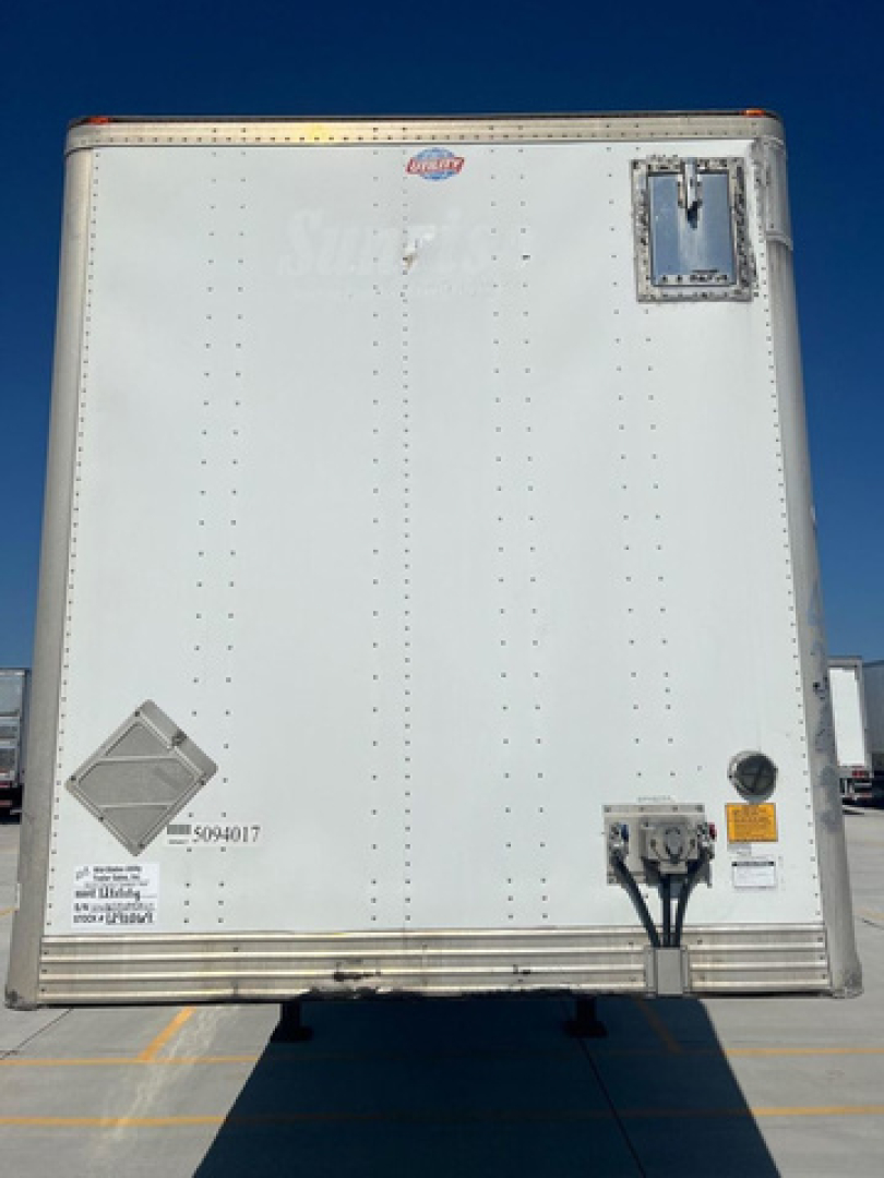 Rear view of a white utility van trailer showing small safety placards, electrical outlets, and a rear door latch; no legible brand names or model numbers readable.