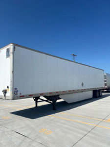 Long white utility trailer viewed from rear-left side showing underside support legs and trailer body with DOT reflectors.