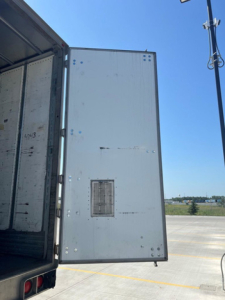 Utility van interior cargo area with open rear door showing metal panel and ventilation grate.
