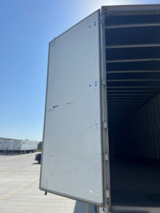 Utility van trailer rear door open showing interior empty cargo space and exterior hinge details.