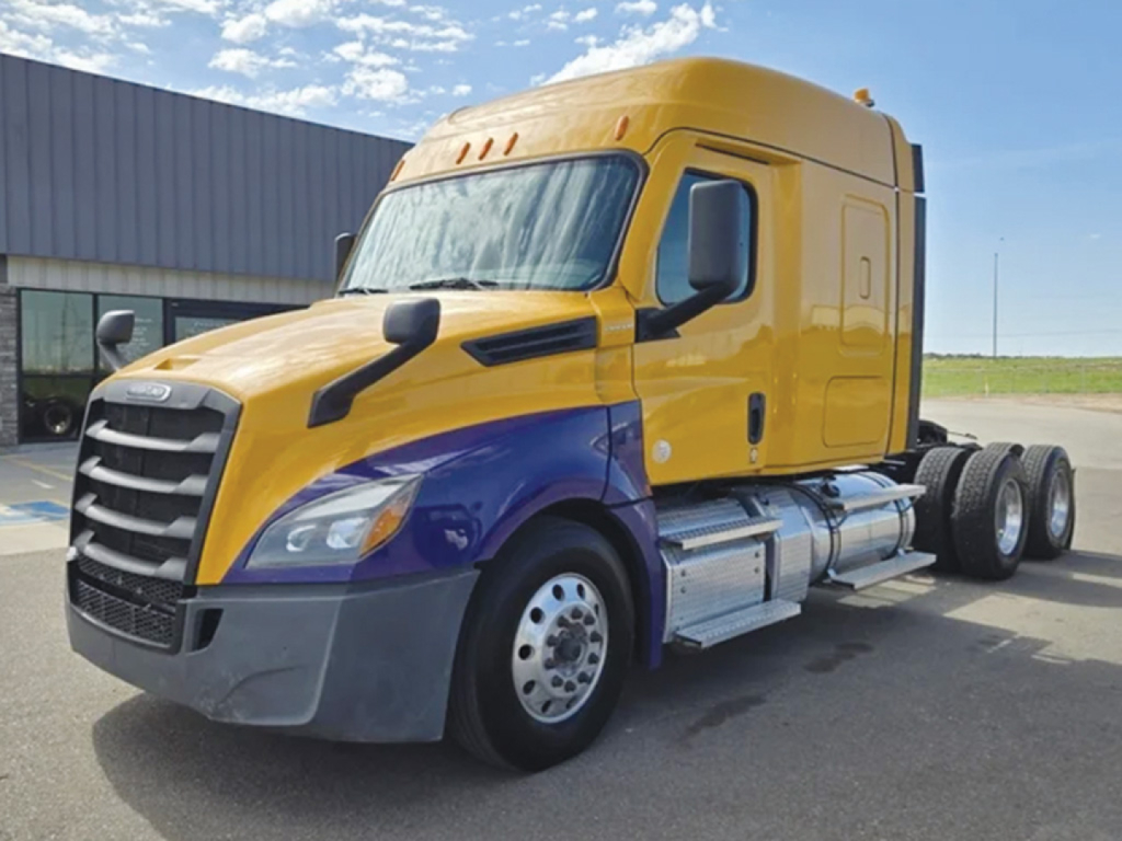 Truck engine bay view of a 2022 Freightliner Cascadia126 sleeper cab with yellow cab and purple lower section, single-axle front, three rear axles, daytime