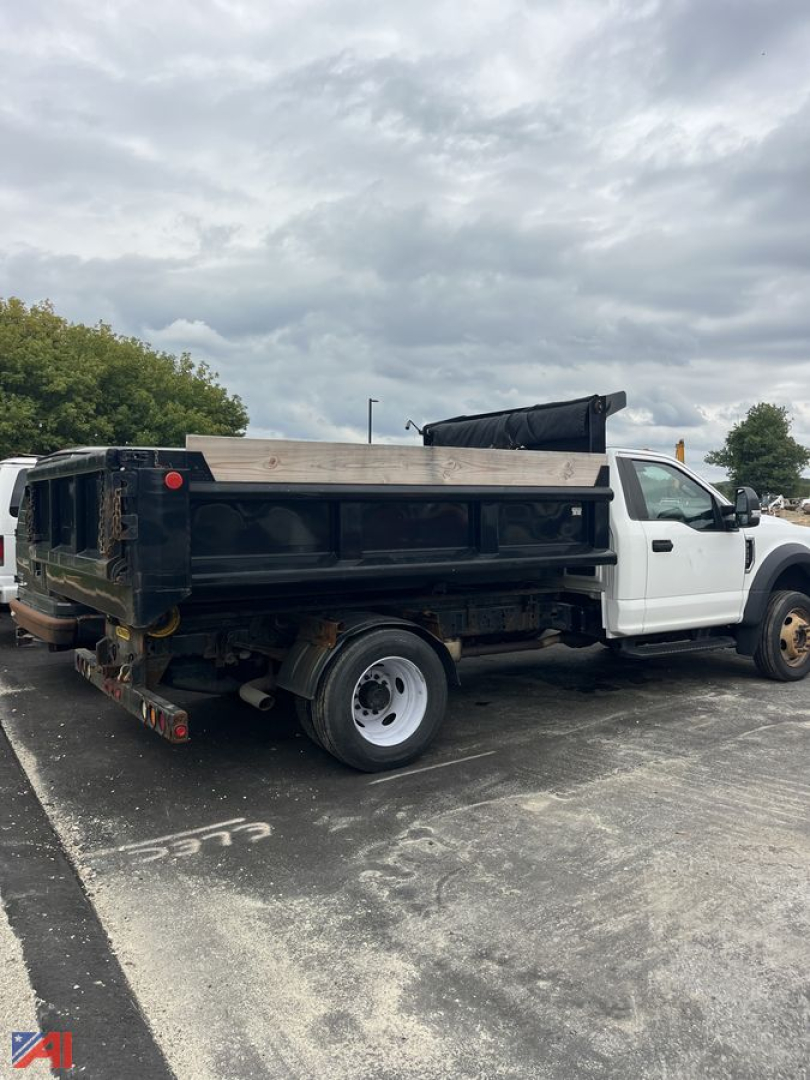 Ford F-550 dump truck in service showing black dump bed and white cab, side view angled rear for-sale vehicle.