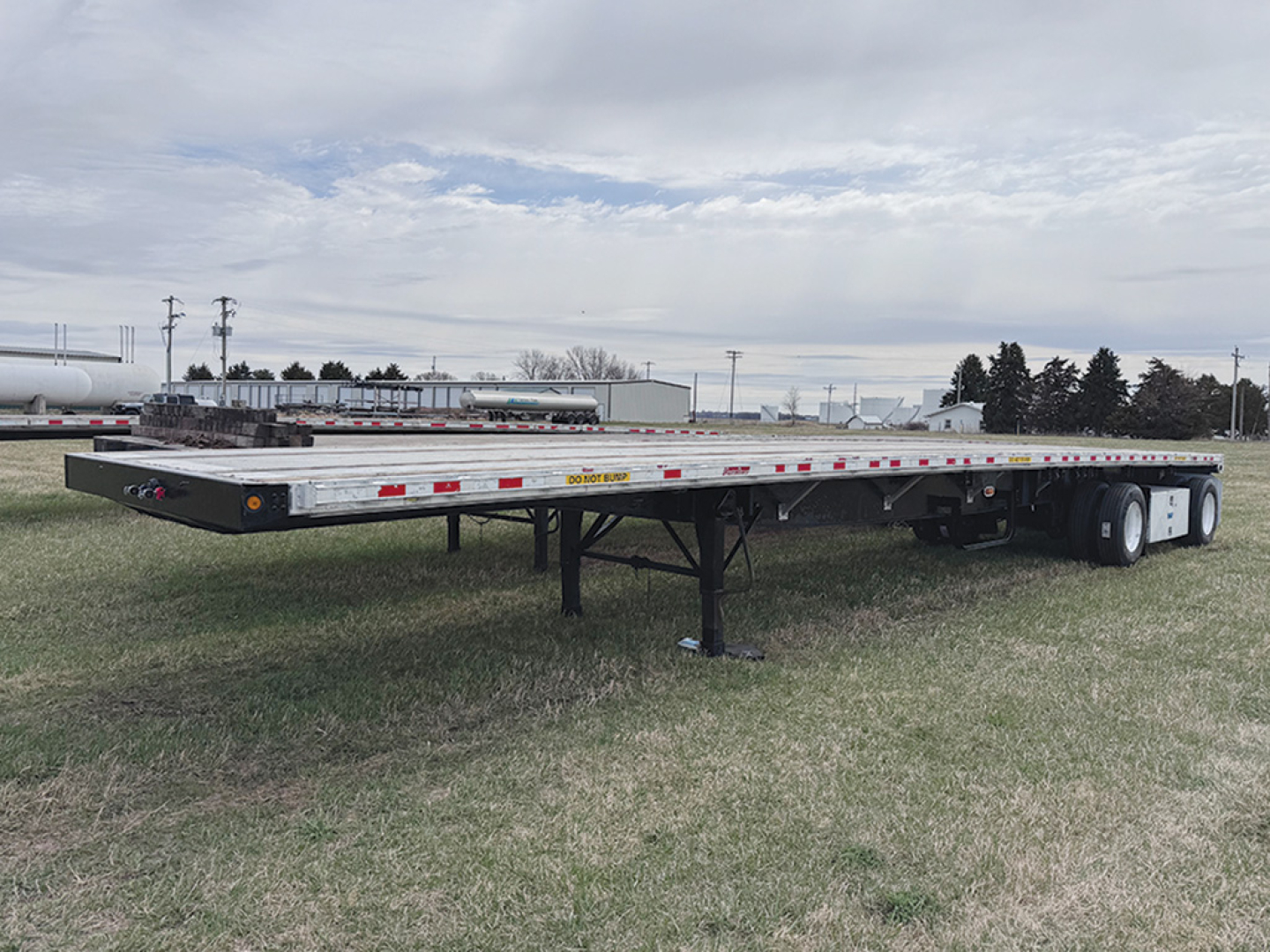 Great Dane flatbed trailer on grass with aluminum and steel composite deck, front landing gear down, rear dual axles, reflective tape along sides.